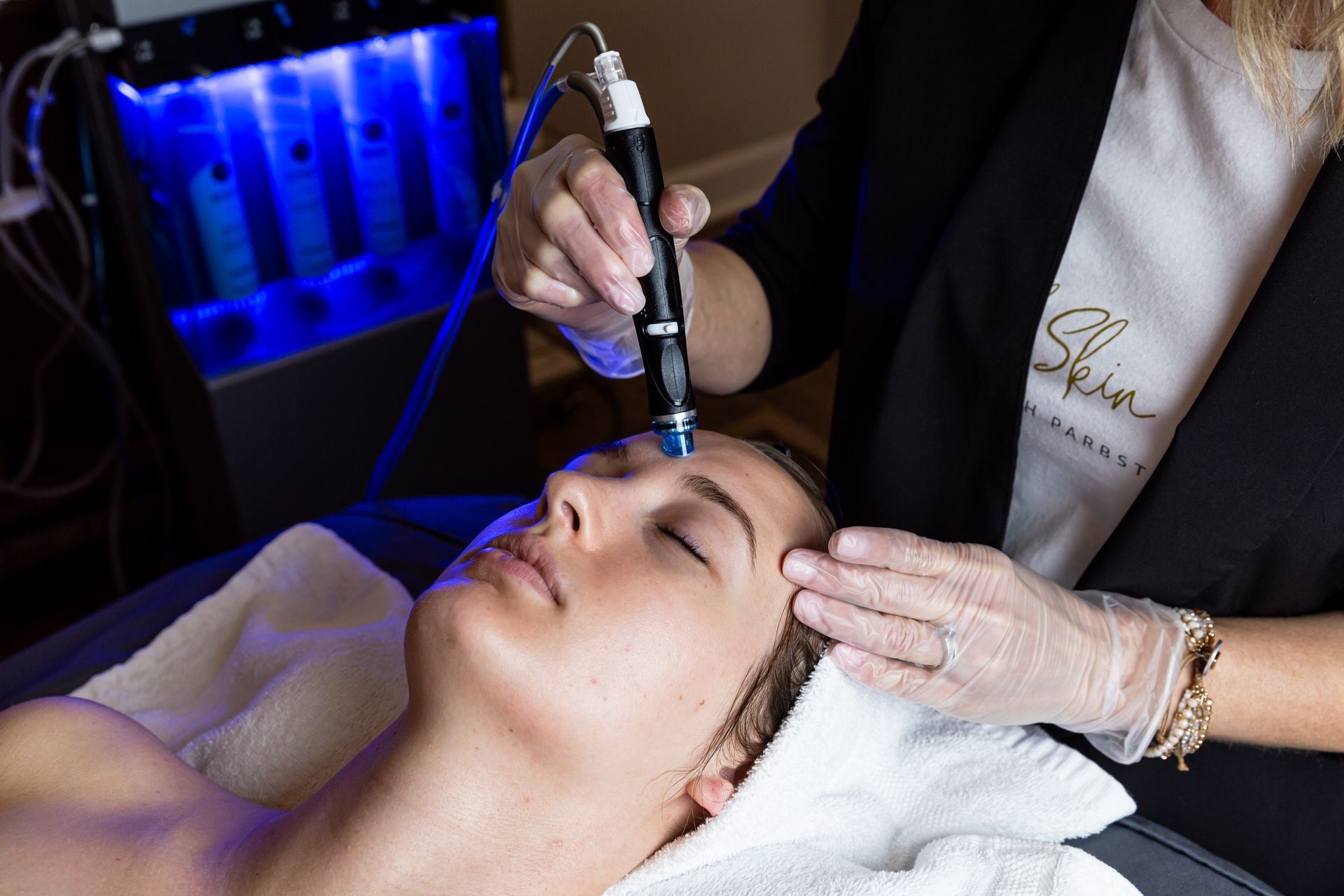 A professional aesthetician uses a handheld skin resurfacing tool on a client's forehead during a facial treatment.