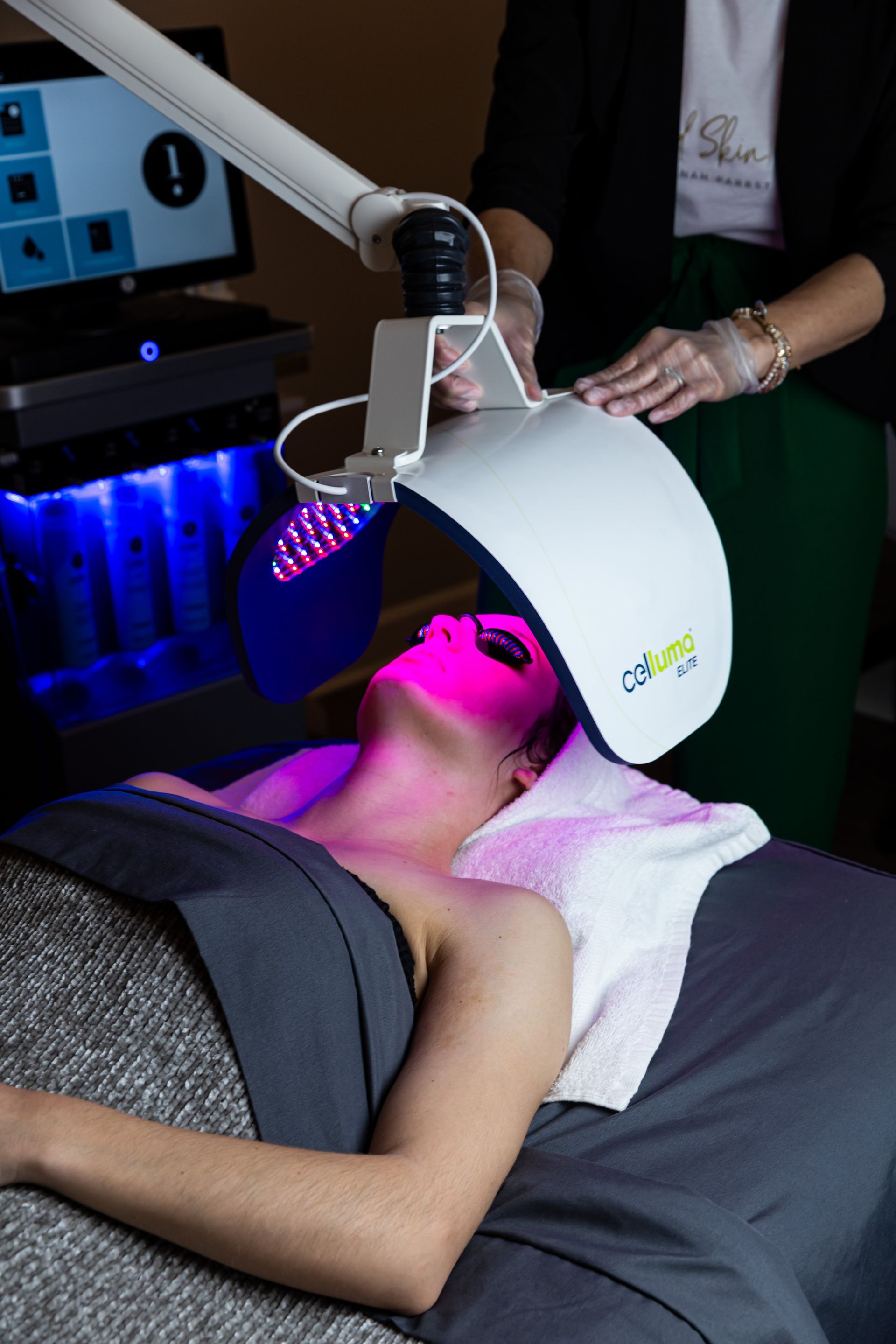 A person lying on a spa bed receives a professional red light therapy treatment from a technician using a Celluma device.