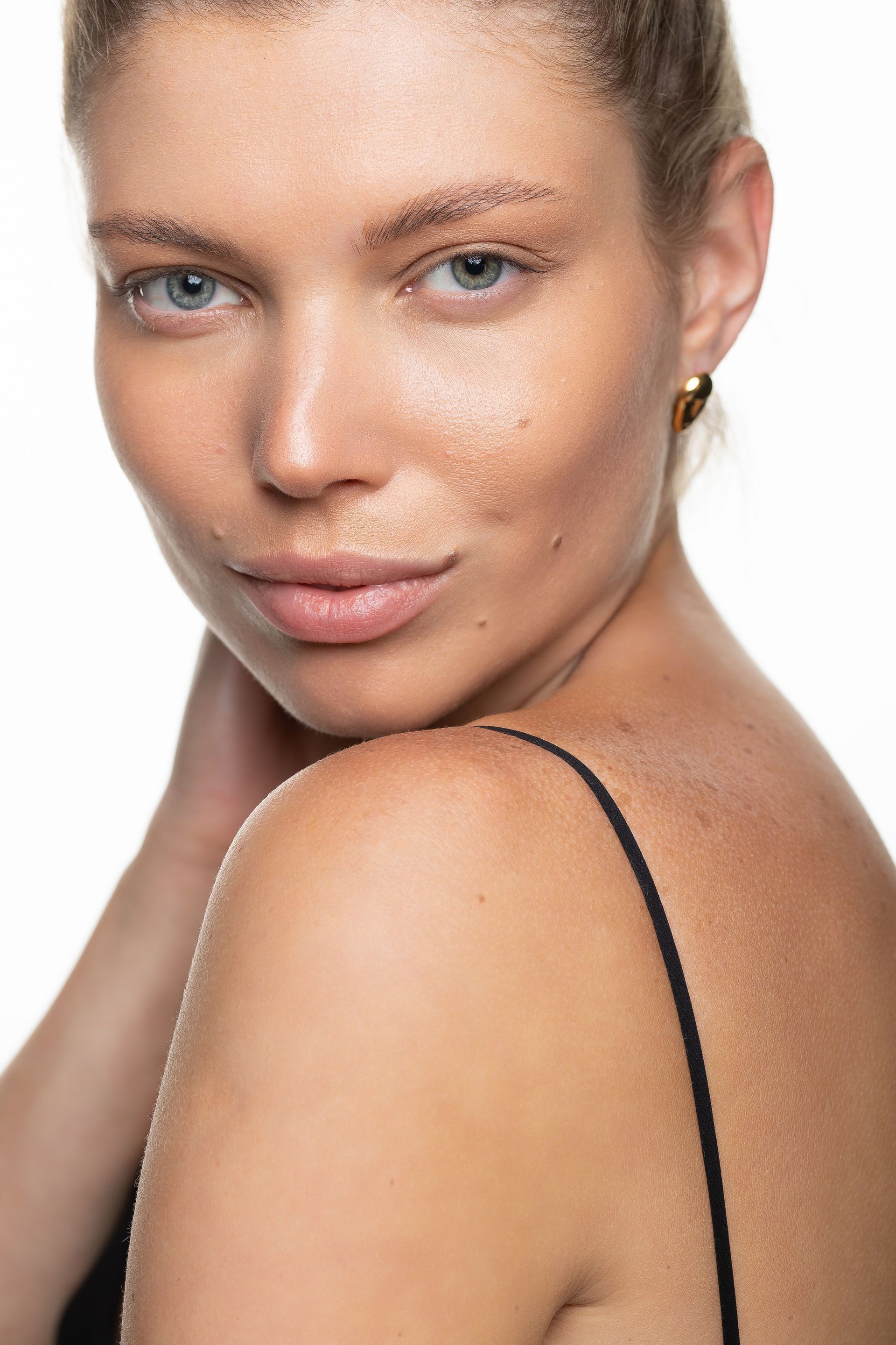Close-up portrait of a person with freckles and light eyes, posing with their shoulder forward against a white background.