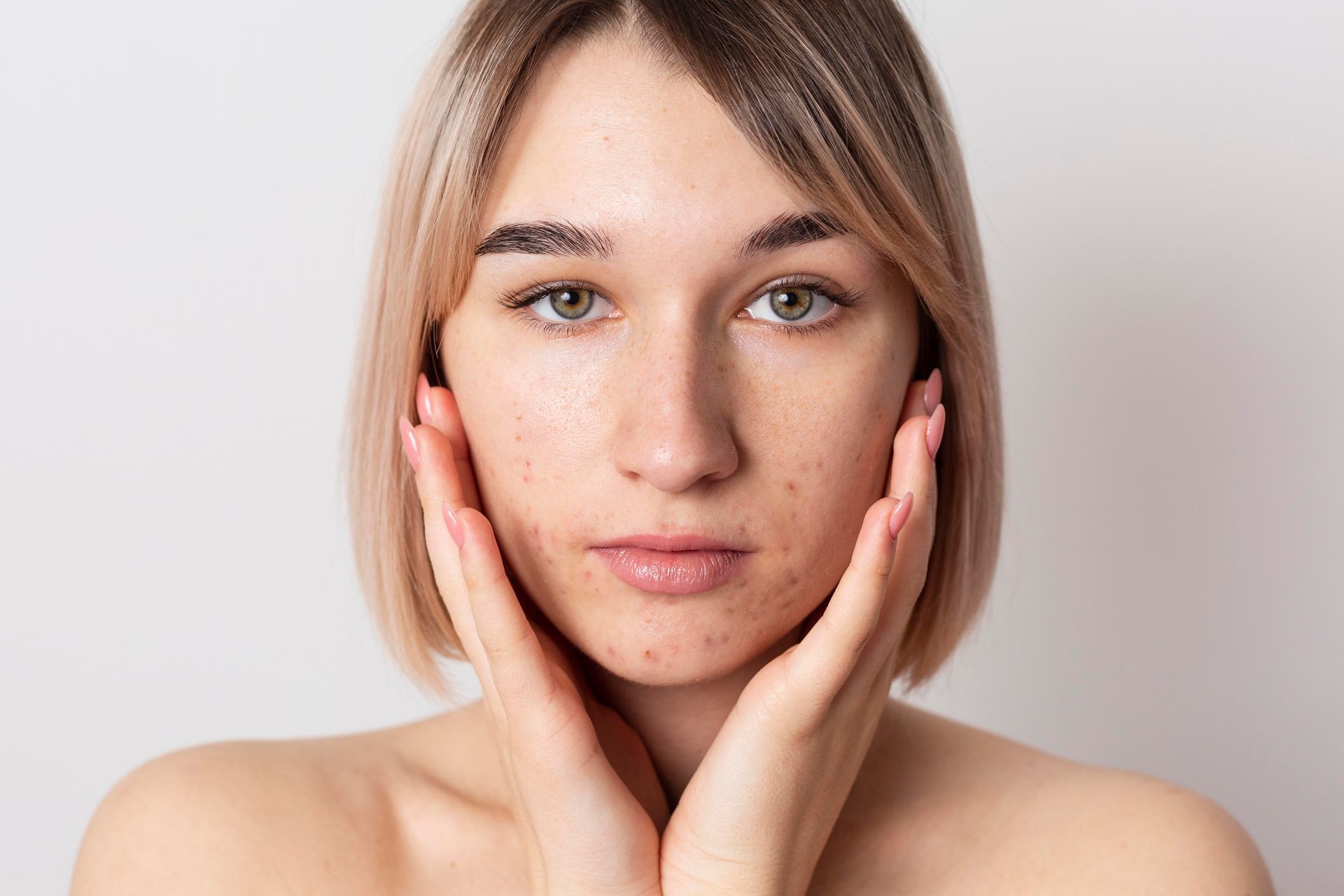 A person with glowing, dewy skin gently touches their face with both hands against a plain, light background.