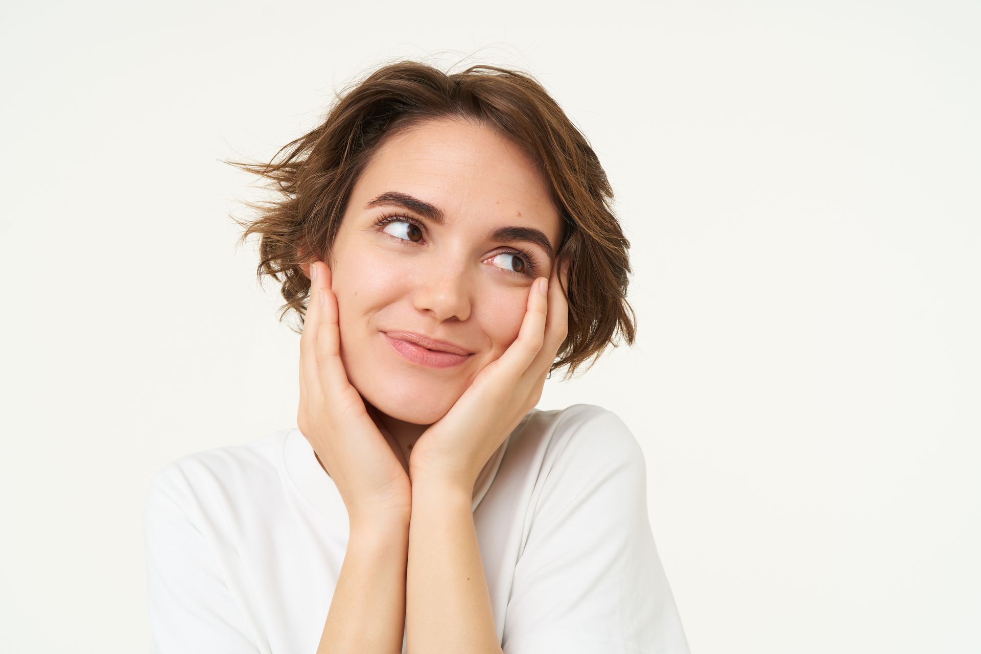 A person with short brown hair rests their face on their hands, looking off to the side with a gentle smile.