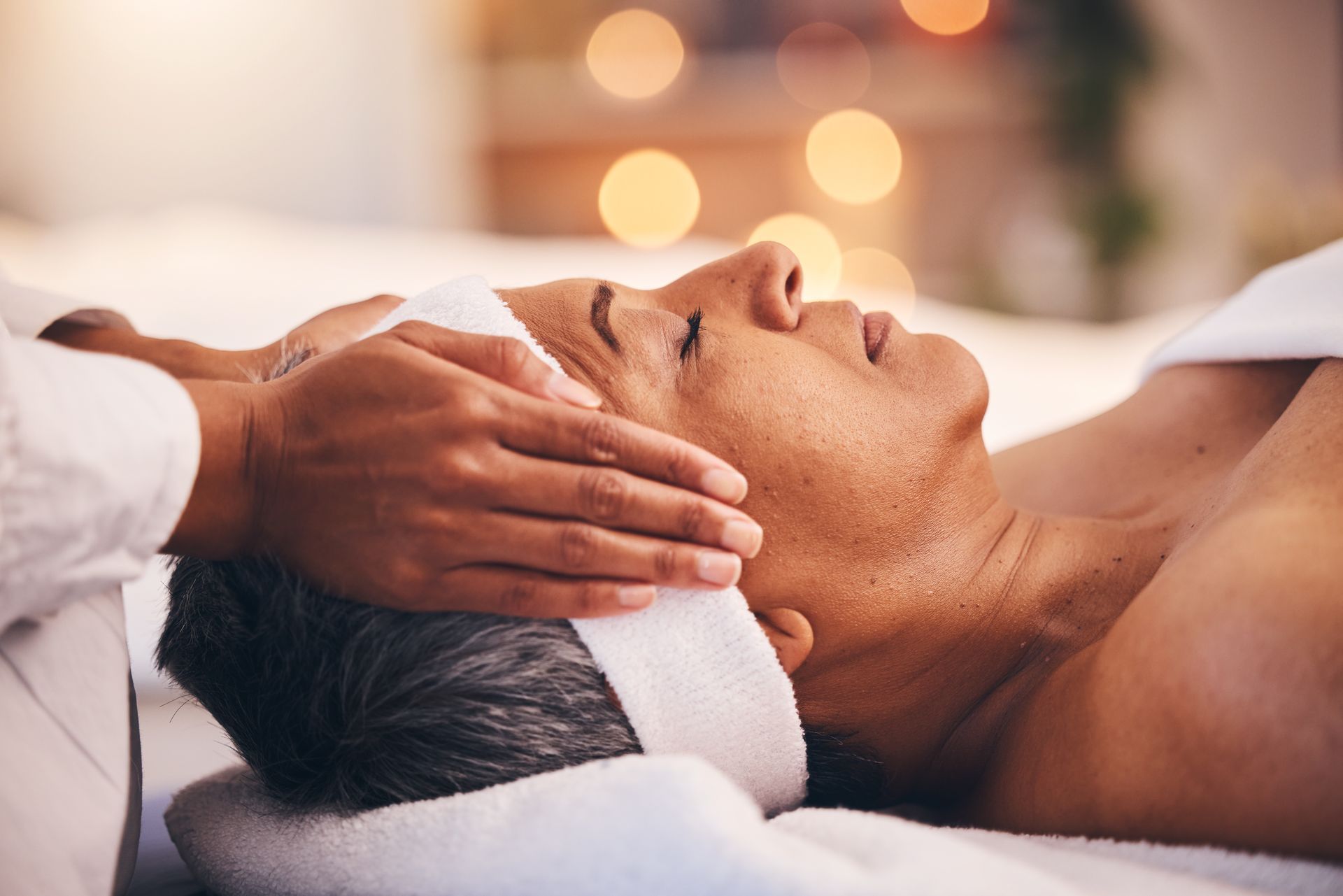 A person receives a gentle face massage in a spa setting with soft, glowing lights in the background.