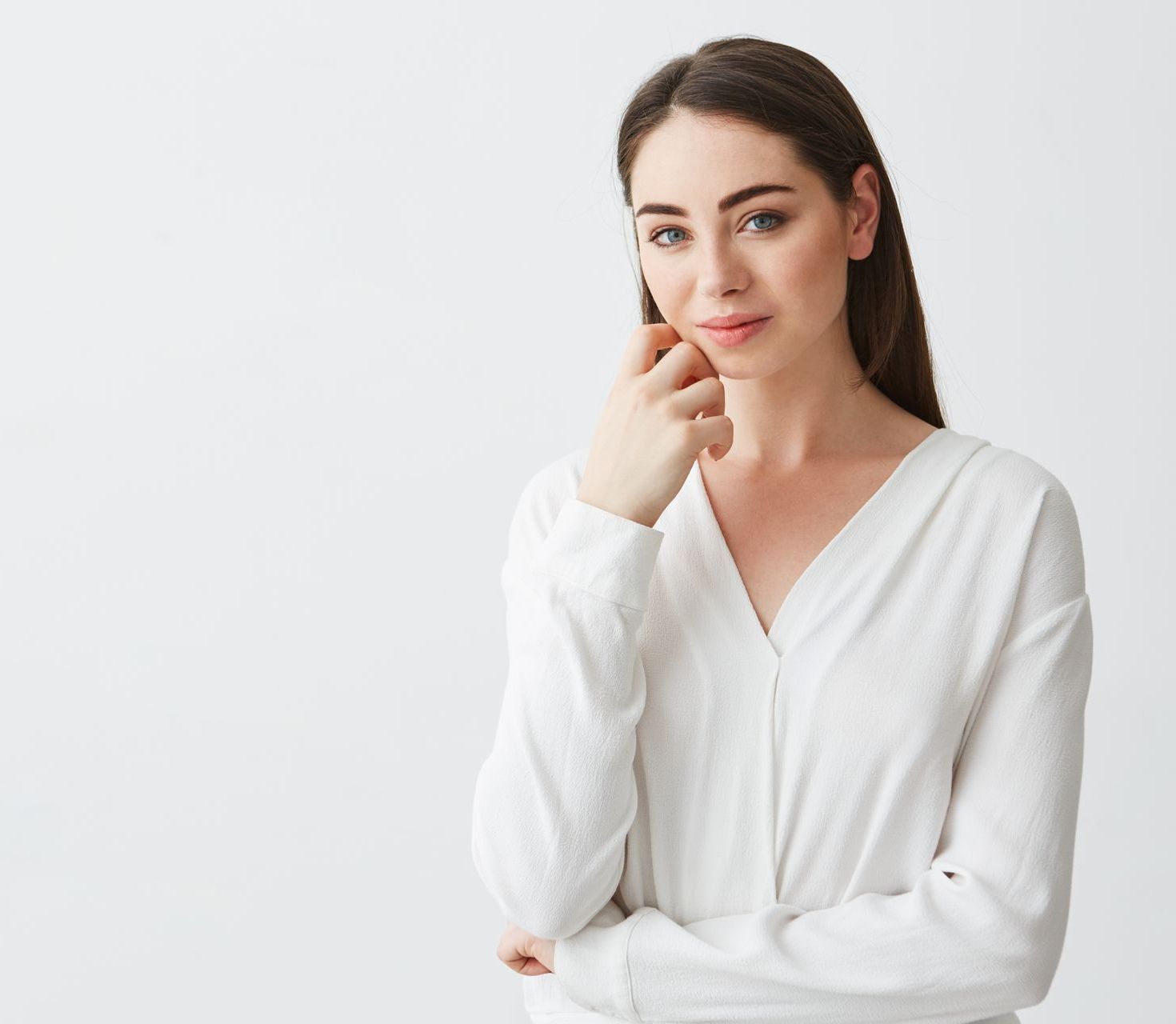 A person wearing a white long-sleeved shirt with a V-neck, resting their chin on their hand against a plain background.