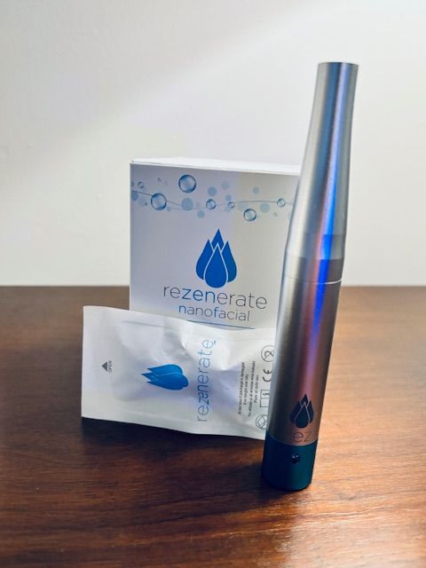 A silver Rezenerate nanofacial handheld device stands next to its branded product box and a sealed package on a wooden table.