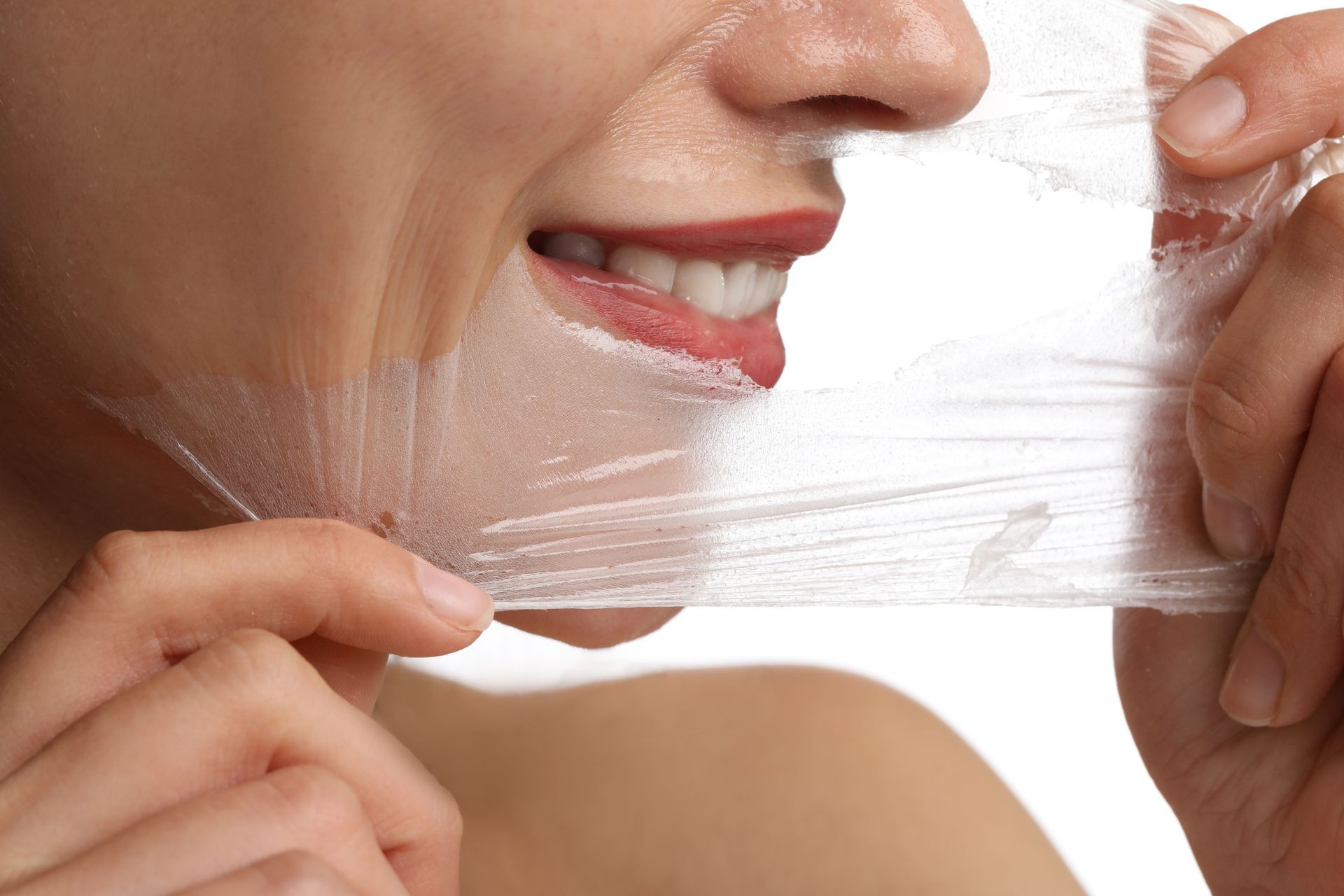 A person’s hand peels a clear, thin mask off their face, revealing smooth skin underneath.