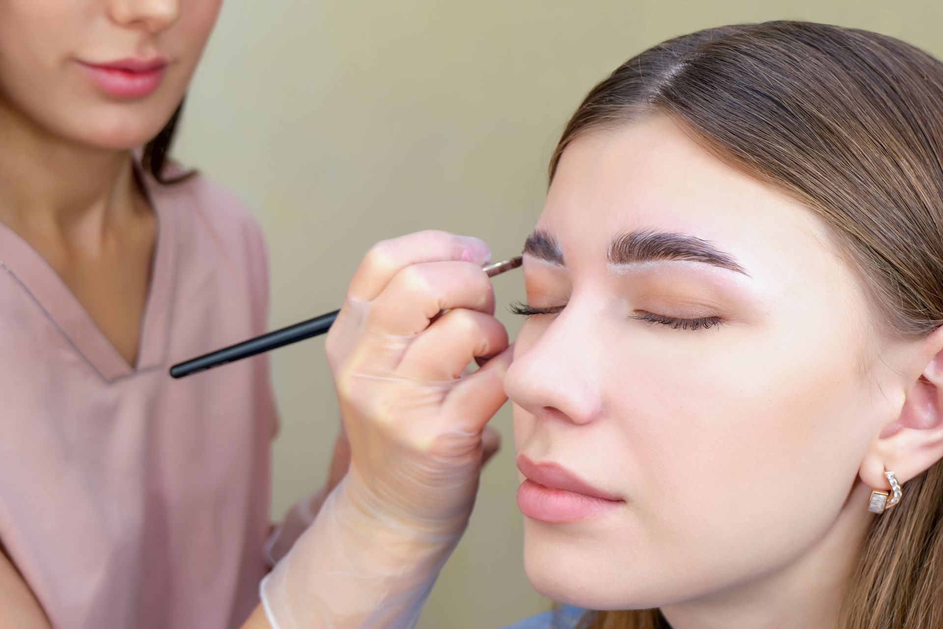 A professional applies makeup to a client's eyebrow using a small brush.