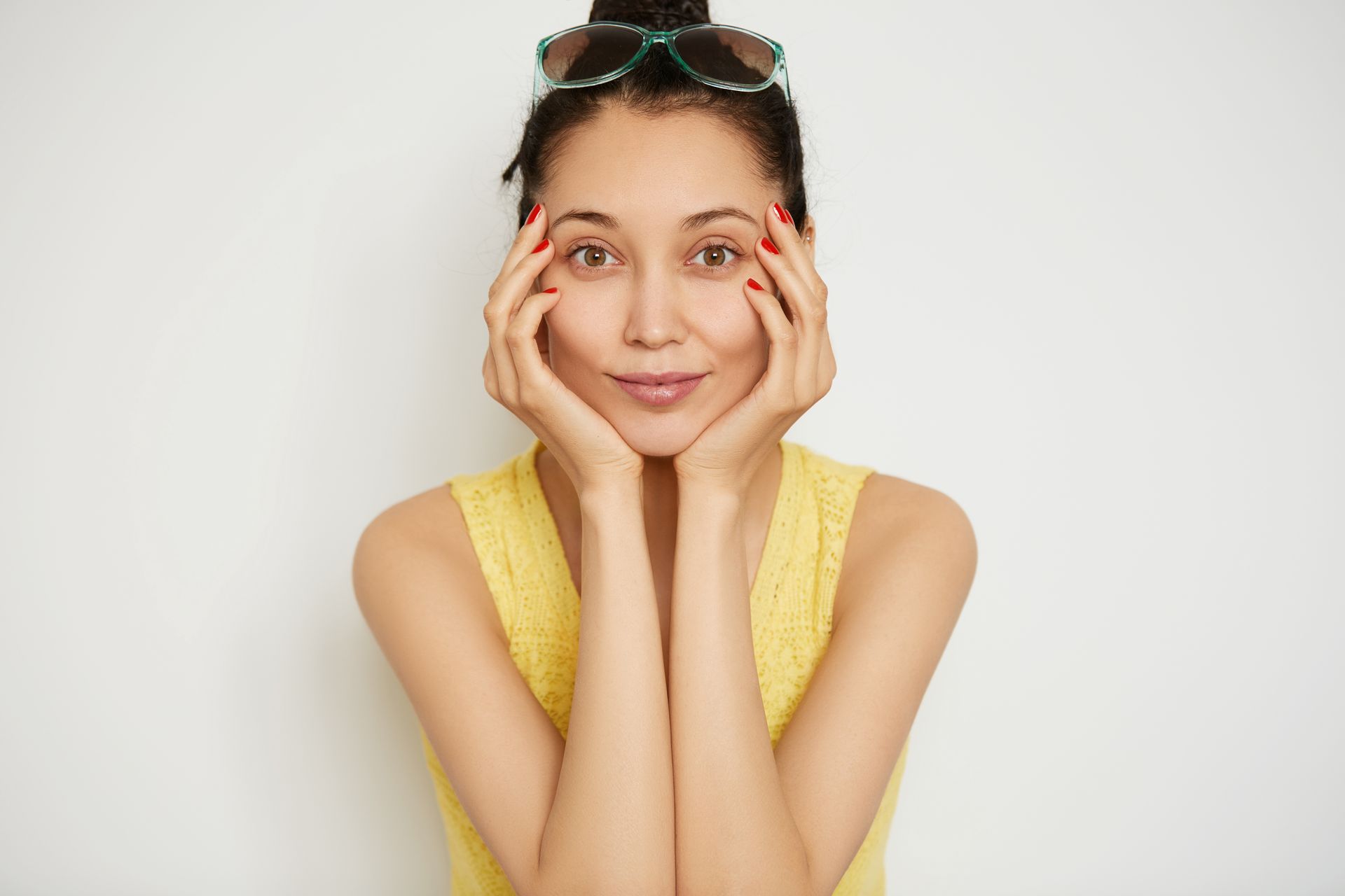 A person in a yellow top and sunglasses perched on their head rests their face in their hands, looking at the camera.