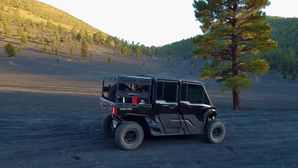 Black off-road vehicle driving on dark terrain near a hillside with trees in the background.