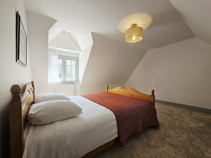 Petite chambre mansardée avec deux lits jumeaux, murs blancs, une fenêtre et un plafonnier.
