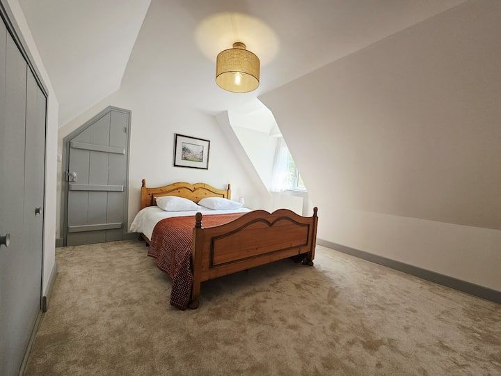 Chambre mansardée confortable avec un lit en bois, de la moquette beige et des murs blancs en pente.