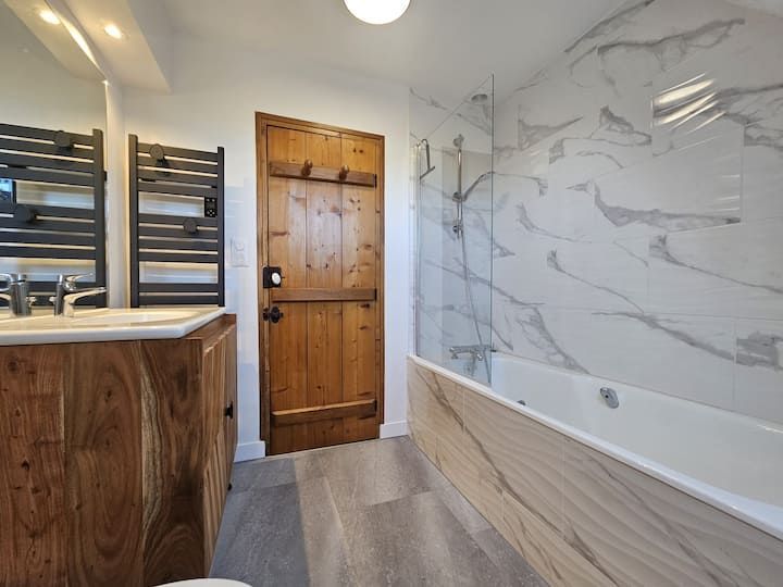 Salle de bains moderne avec meuble-lavabo en bois, douche en verre et porte en bois, murs et sol carrelés gris.