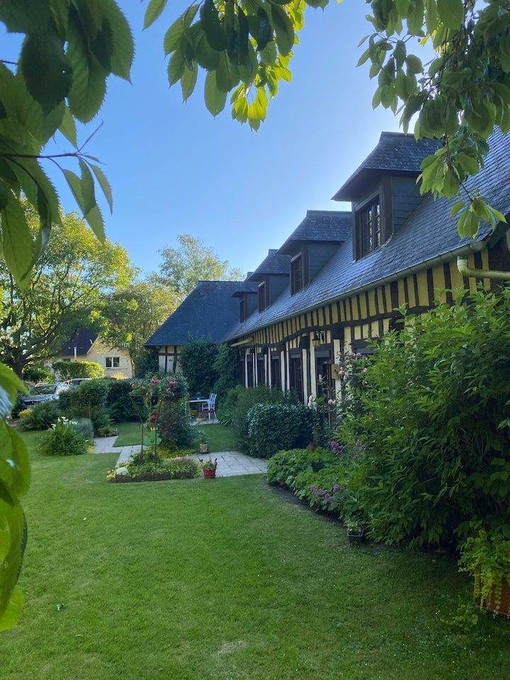 Jardin luxuriant jouxtant une longue maison recouverte de lierre, avec des lucarnes, sous un ciel d'un bleu limpide.