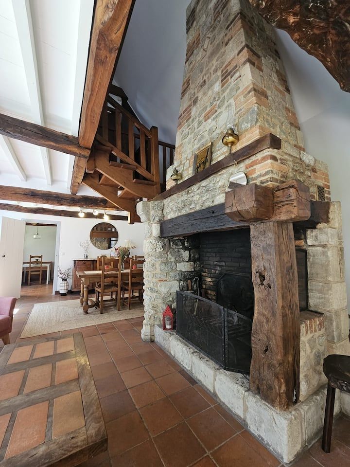 Salle à manger rustique avec une grande cheminée en pierre, des carreaux de terre cuite et des poutres en bois apparentes.