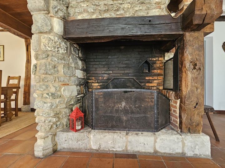Cheminée rustique en pierre avec foyer en fer noir et lanterne rouge sur l'âtre.