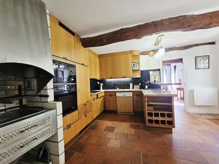Cuisine rustique avec placards en bois, sol carrelé, cuisinière, îlot central et petite fenêtre près de l'évier.