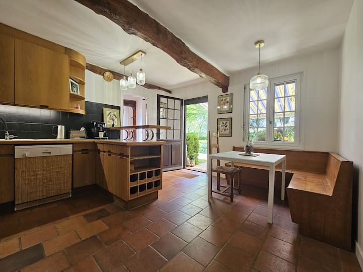Cuisine-salle à manger chaleureuse avec placards en bois, sol en terre cuite et porte ouverte sur une vue sur le jardin