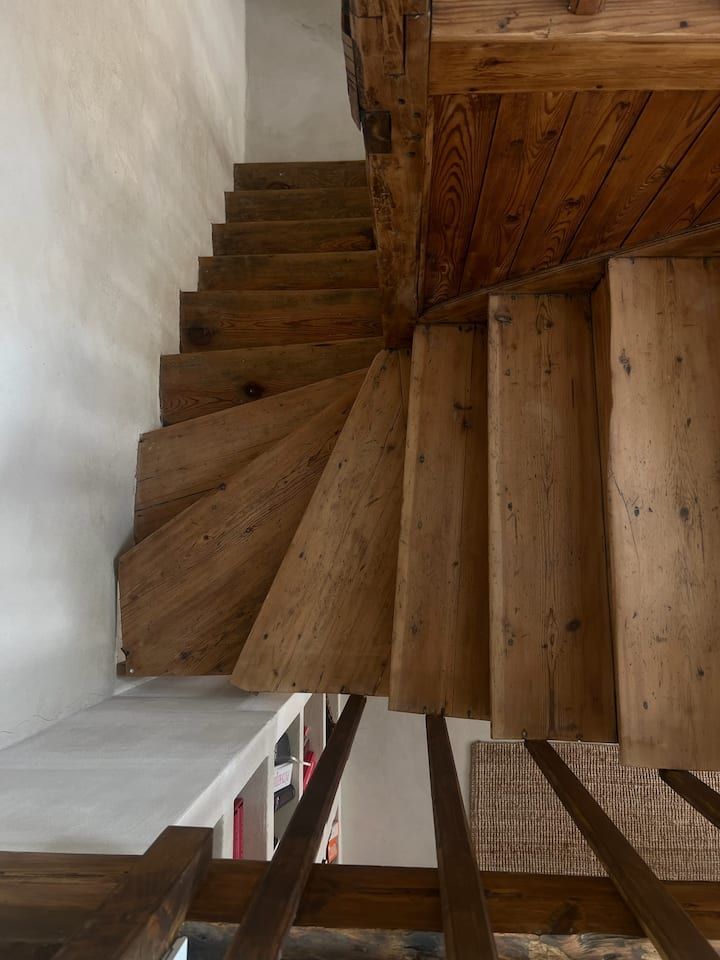 Escalier en colimaçon en bois vu d'en bas, avec murs blancs et sol carrelé.