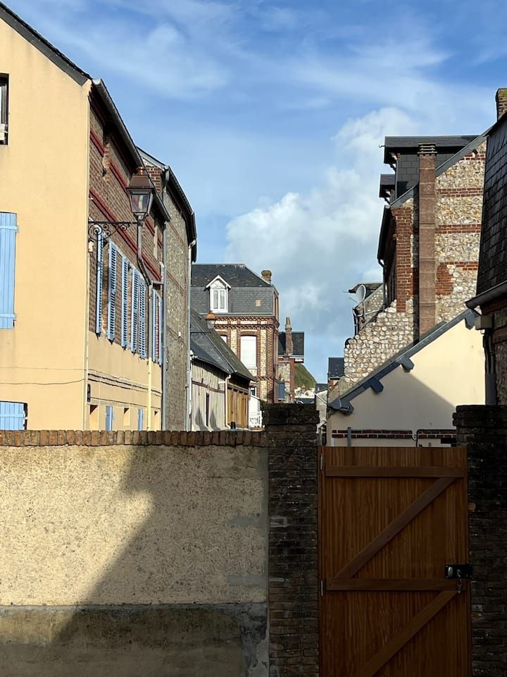 Ruelle étroite entre des bâtiments en briques, avec un portail en bois et un ciel bleu au-dessus.
