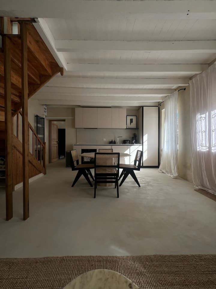 Coin repas minimaliste avec table et chaises, escalier et petite cuisine dans un loft lumineux