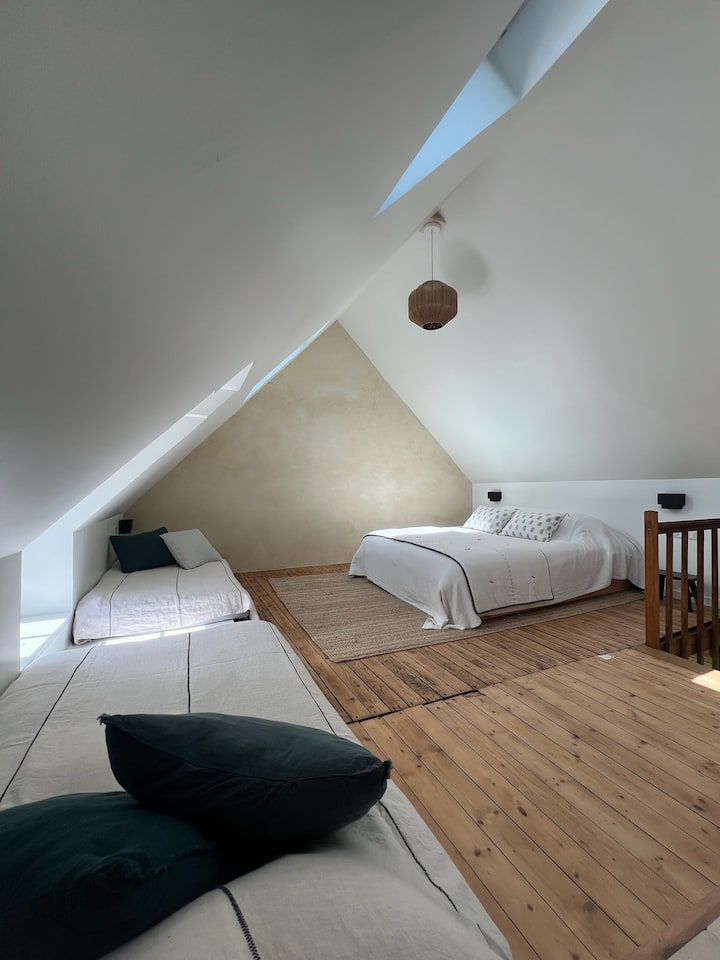 Chambre mansardée avec plafond blanc en pente, deux lits simples et un plancher en bois