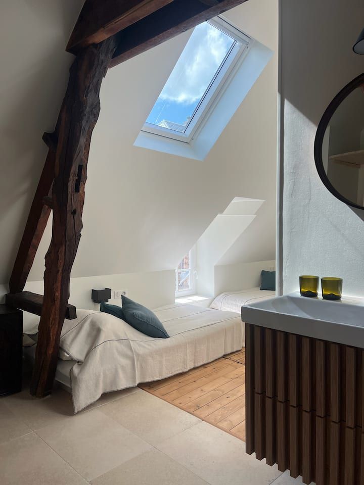 Chambre mansardée lumineuse avec puits de lumière, lit simple et mur en bois près d'un petit bureau.