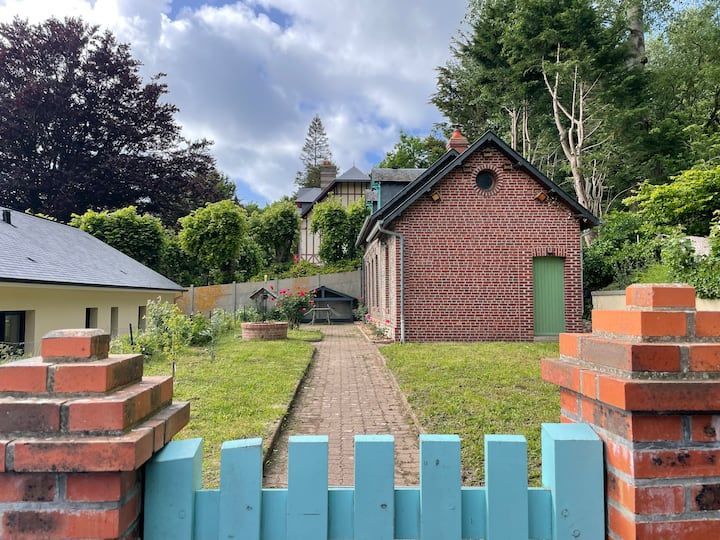 Allée de jardin en briques menant à un petit cabanon en briques rouges et à une maison derrière un portail turquoise