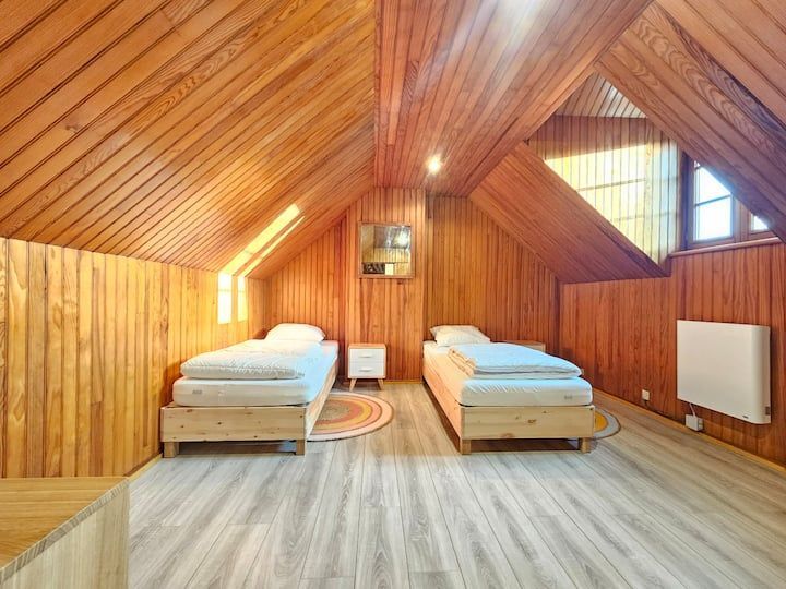 Chambre mansardée confortable en bois avec deux lits simples, plafond mansardé, fenêtre et radiateur