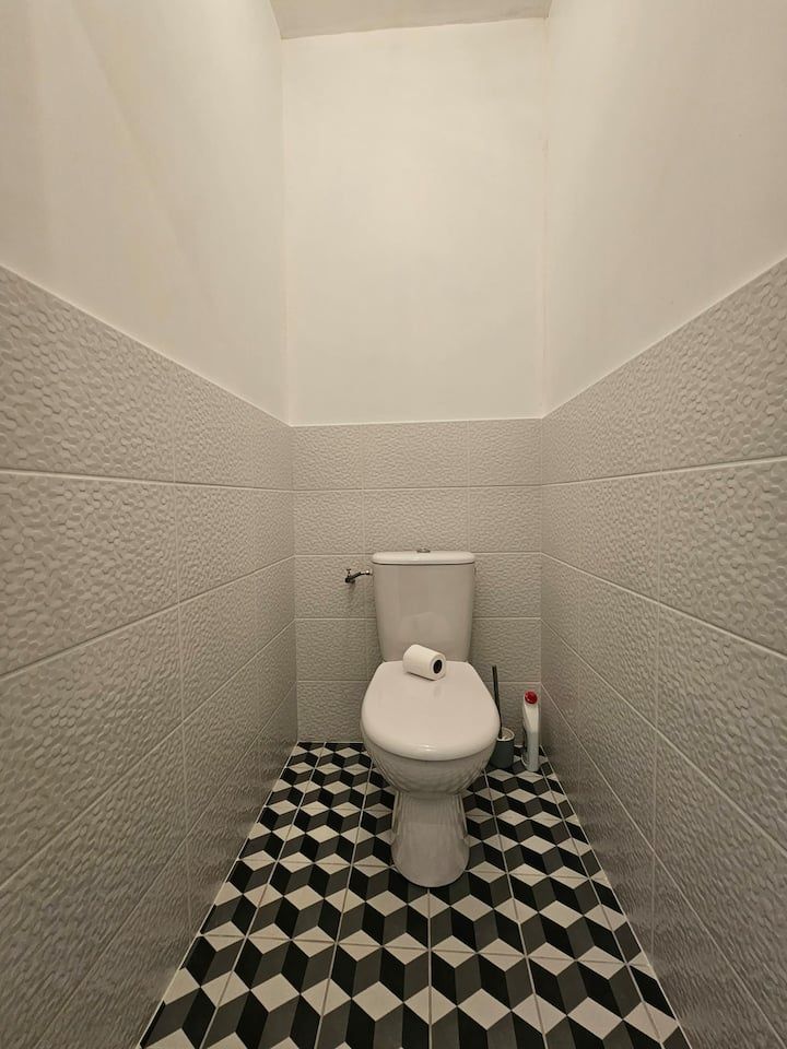 Petite salle de bains carrelée avec toilettes, murs blancs et sol à motifs noirs et blancs.