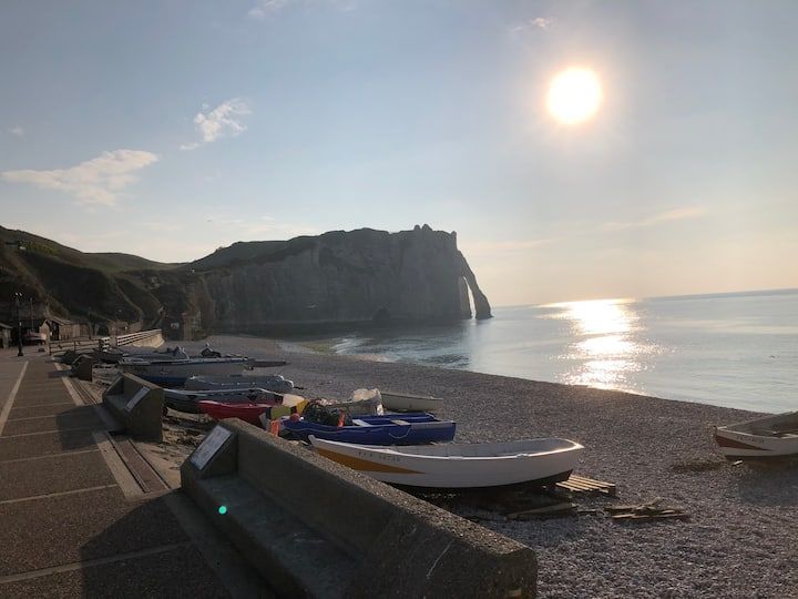 Plage de galets avec de petits bateaux, digue et coucher de soleil sur les falaises côtières.