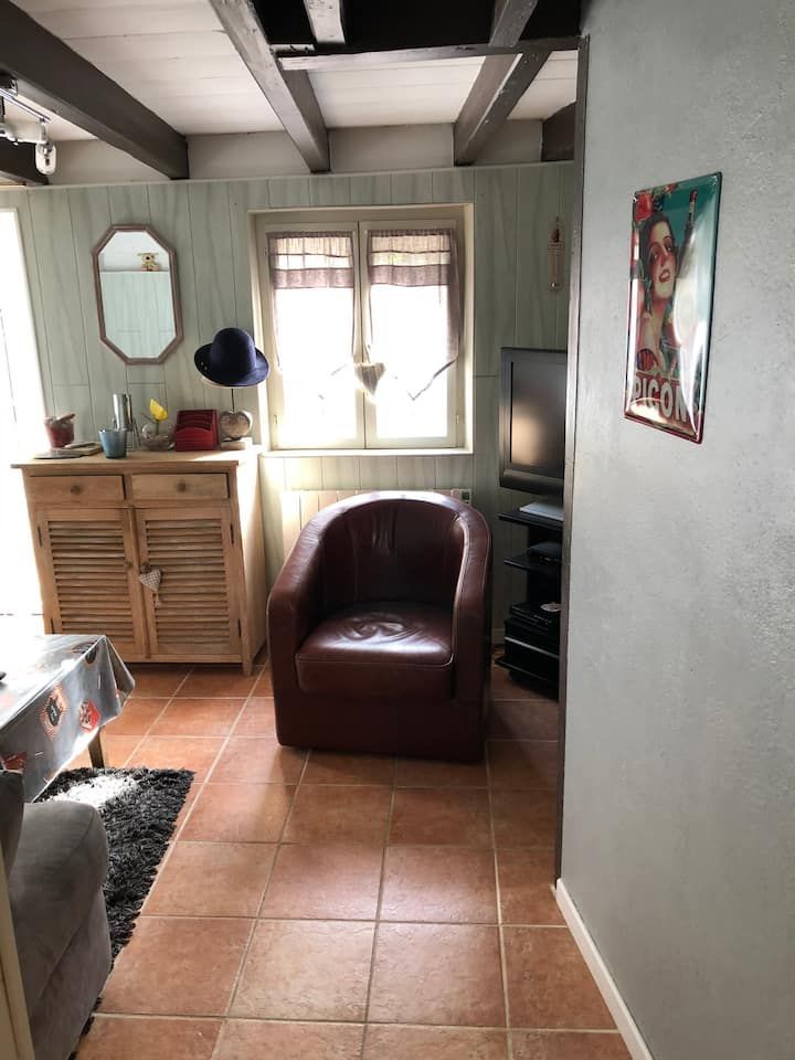 Petit salon avec sol en carrelage de terre cuite, fauteuil en cuir, fenêtre, armoire et décoration murale.