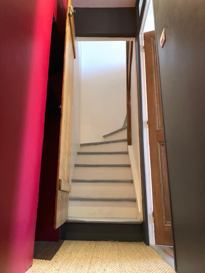 Escalier étroit aux marches blanches, murs brun foncé et mur rouge sur la gauche.