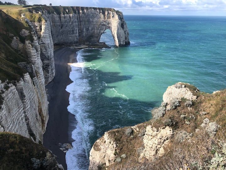 Côte escarpée aux falaises de craie blanche, mer turquoise et vagues sous un ciel nuageux
