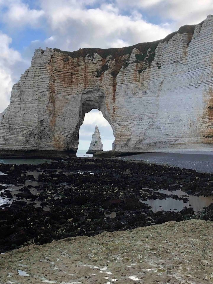 Falaise blanche surplombant une côte rocheuse sombre sous un ciel nuageux, avec une arche naturelle.