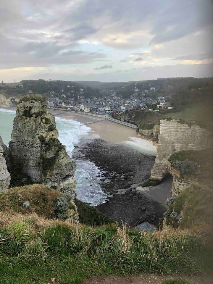 Falaises surplombant une plage en forme de croissant et un village balnéaire sous un ciel nuageux