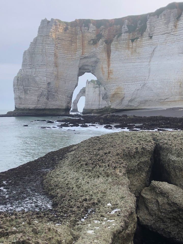 Falaise blanche surplombant une côte rocheuse et des eaux calmes, avec une arche naturelle.