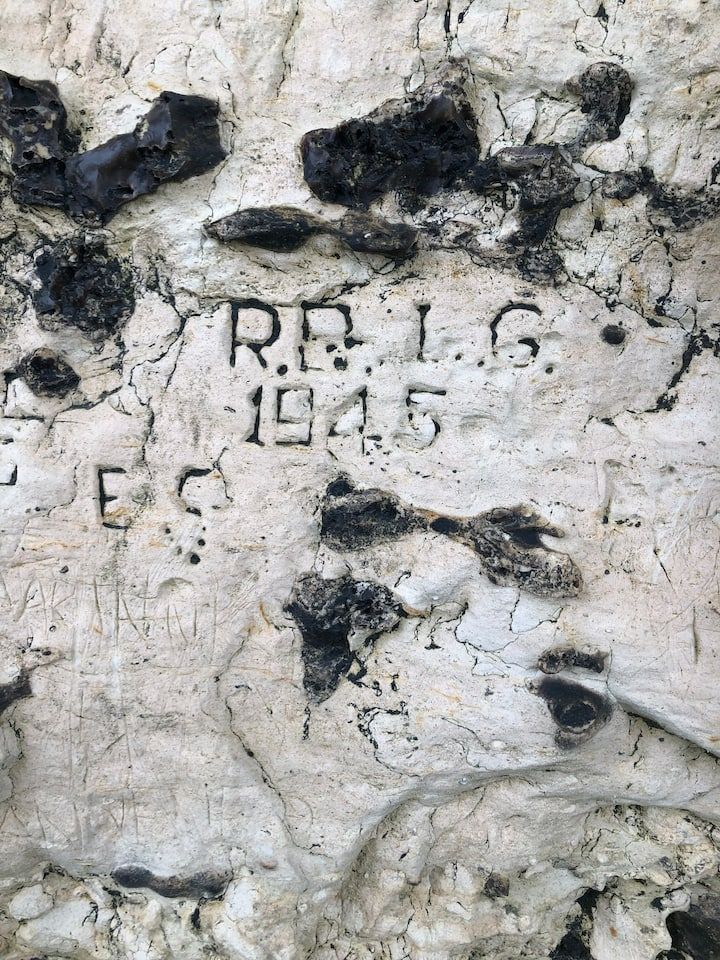 Gros plan sur un mur de pierre érodé par le temps, portant des marques noires et une inscription gravée indiquant « REG 1945 ».