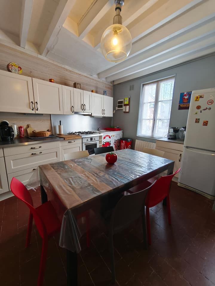 Cuisine lumineuse avec table à manger en bois, chaises rouges, placards blancs et une fenêtre à côté du réfrigérateur.