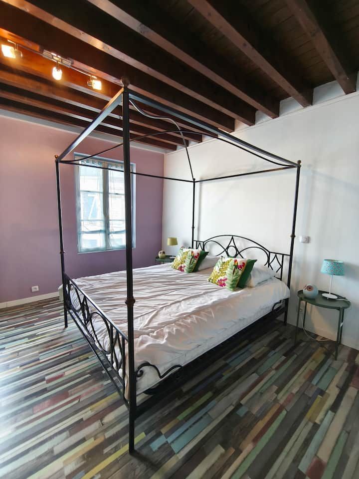 Lit à baldaquin dans une chambre lumineuse avec poutres apparentes et moquette à rayures.