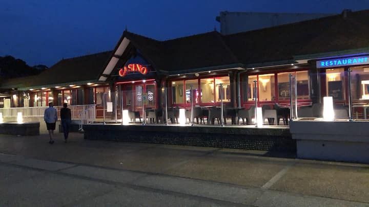 Vue nocturne d'un immeuble éclairé par une enseigne rouge au néon, avec quelques passants à l'extérieur.