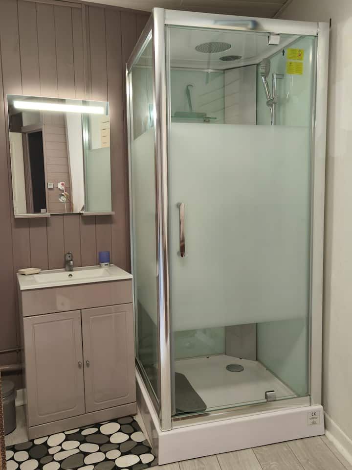 Salle de bains avec meuble-lavabo, miroir et cabine de douche vitrée avec panneaux inférieurs dépolis.
