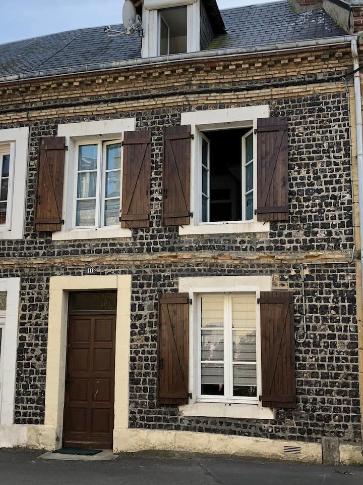 Façade d'une maison en pierre avec des volets bruns et une porte en bois foncé, vue de la rue