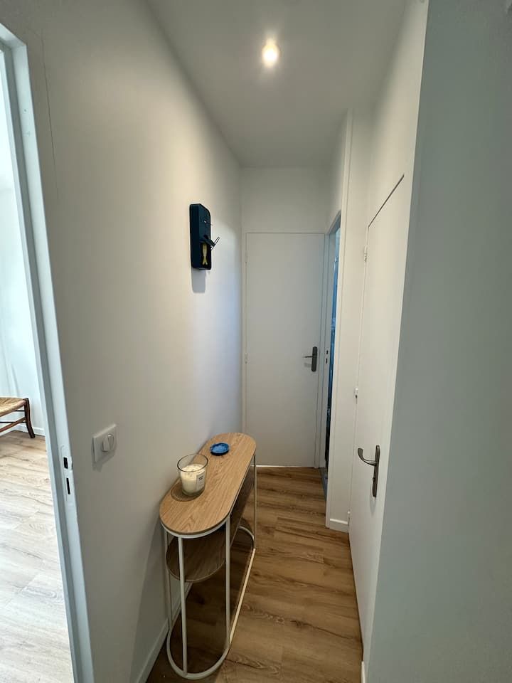 Couloir étroit et blanc avec parquet, petite console, applique murale et porte fermée au fond.