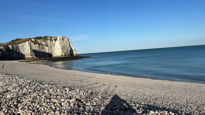 Plage rocheuse bordant une mer bleue calme, avec des falaises blanches sous un ciel dégagé.