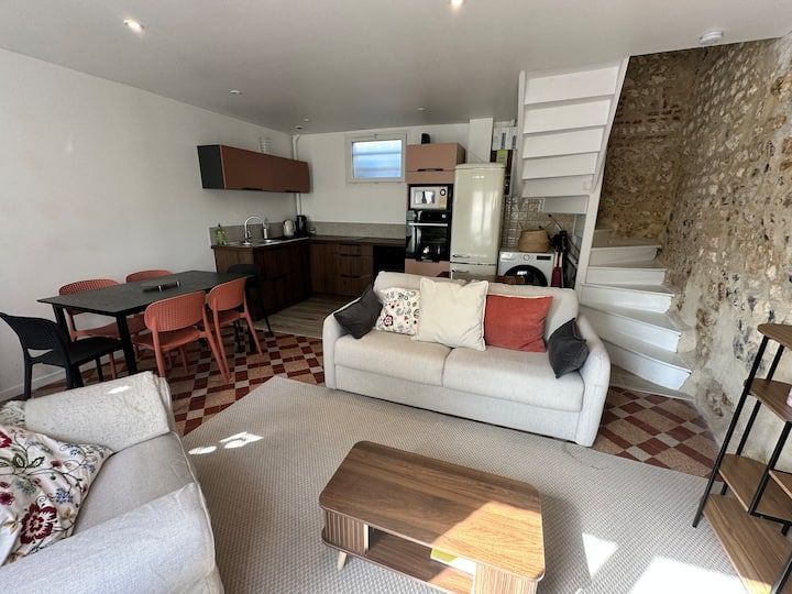 Salon moderne avec canapé, table basse, coin repas, cuisine et escalier blanc avec mur en pierre.