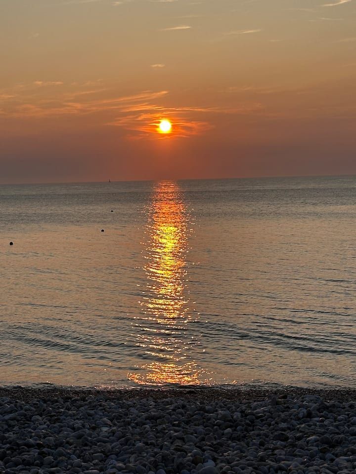 Coucher de soleil sur un océan calme, reflet orangé sur l'eau au-dessus d'une rive rocheuse