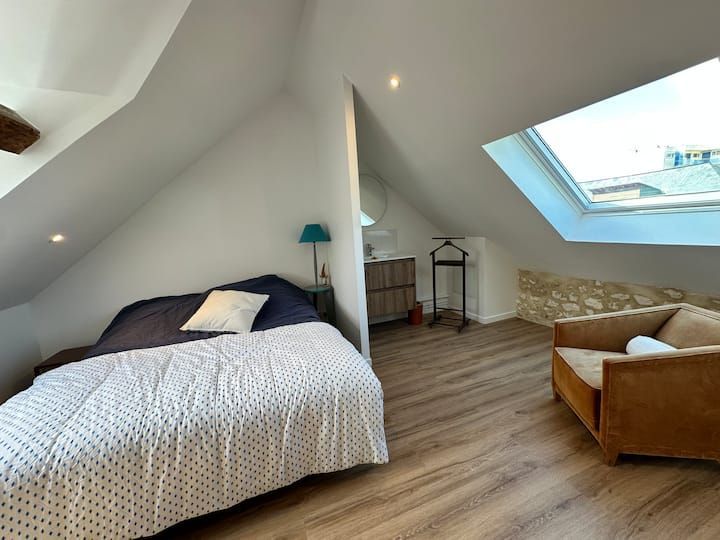 Chambre mansardée lumineuse avec lit, fauteuil, bureau, parquet et fenêtre de toit