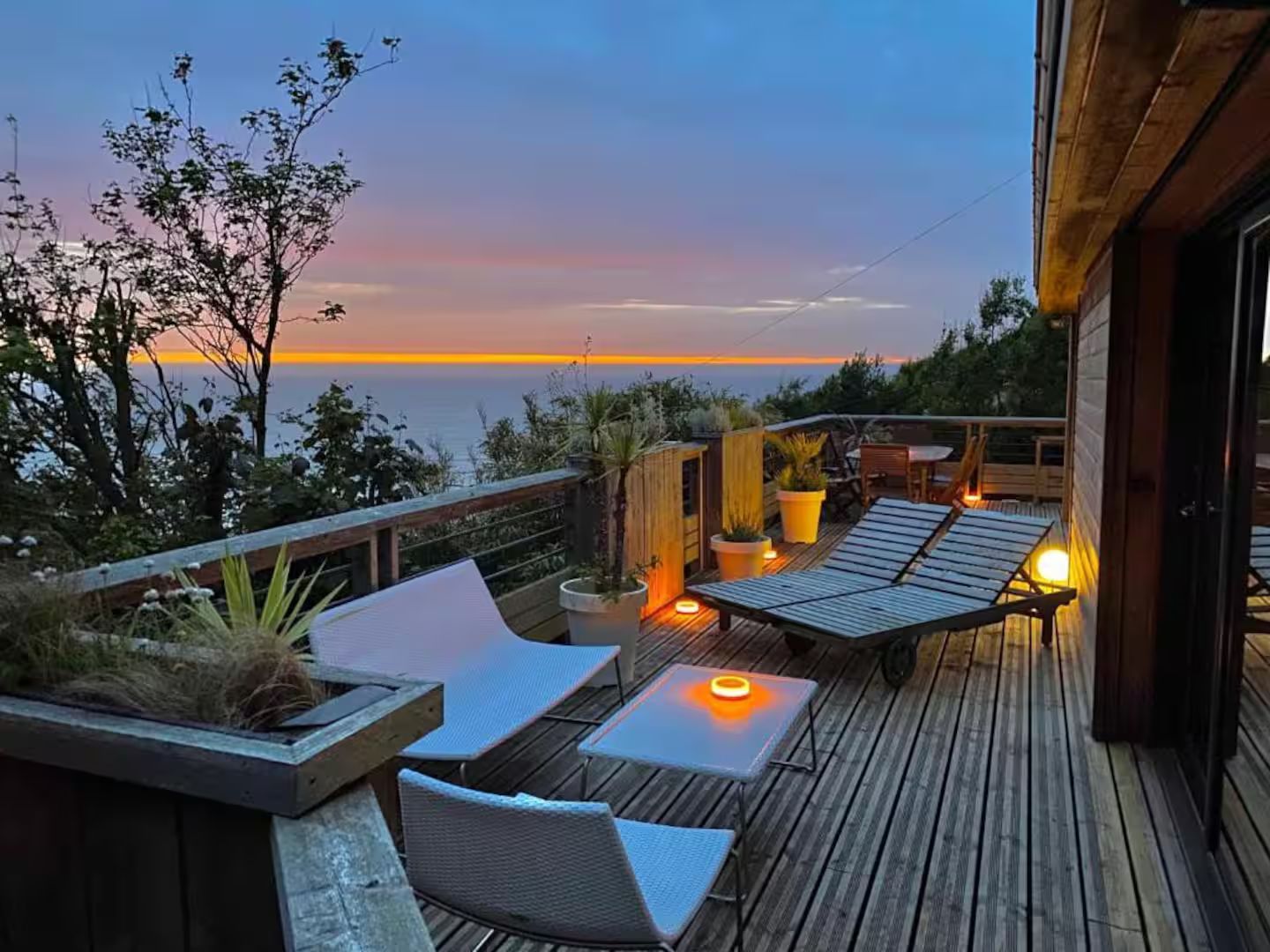 Une terrasse en bois avec des chaises et une table donnant sur l'océan au coucher du soleil.