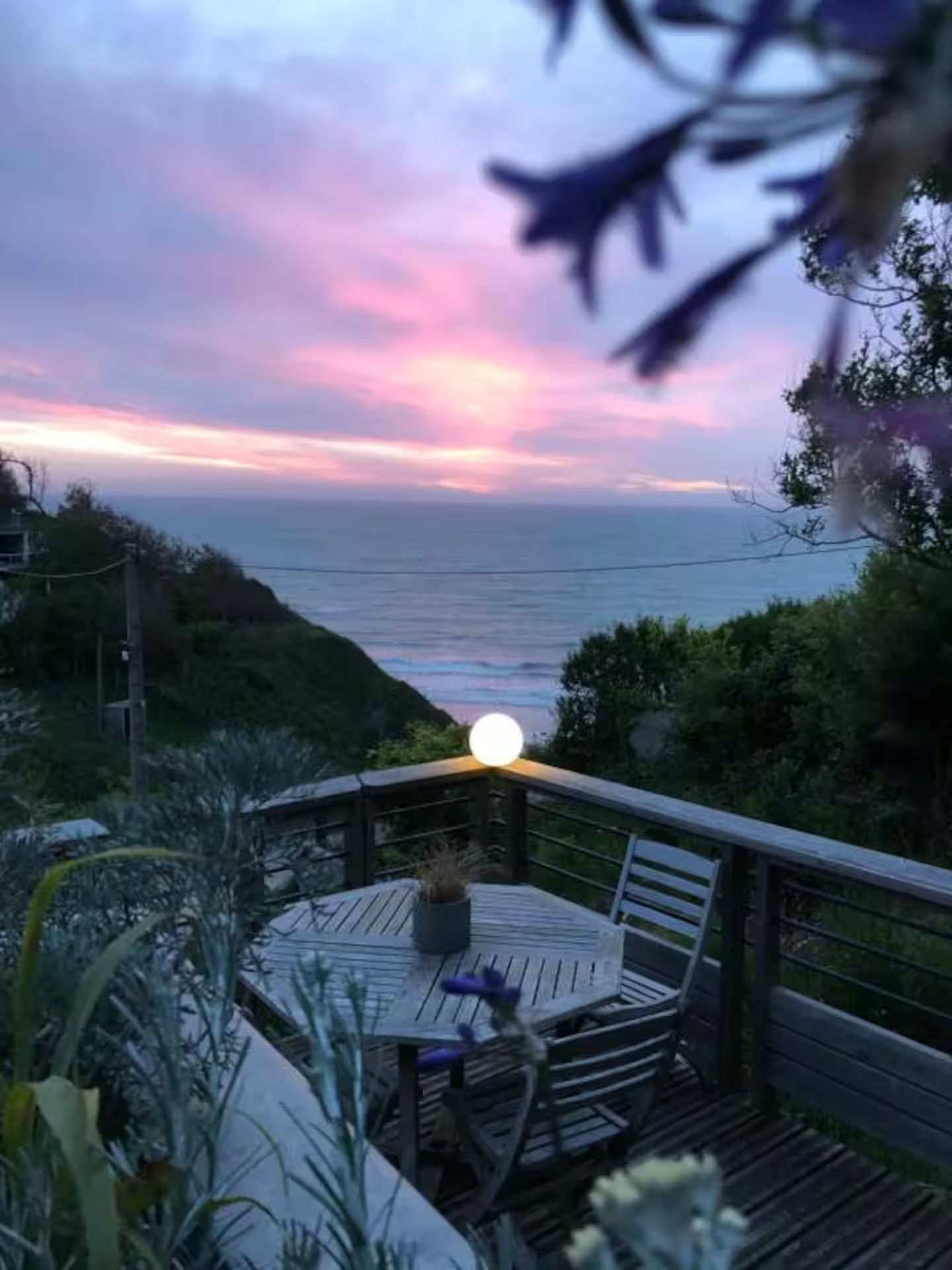 Une table et des chaises sur une terrasse surplombant l'océan au coucher du soleil.