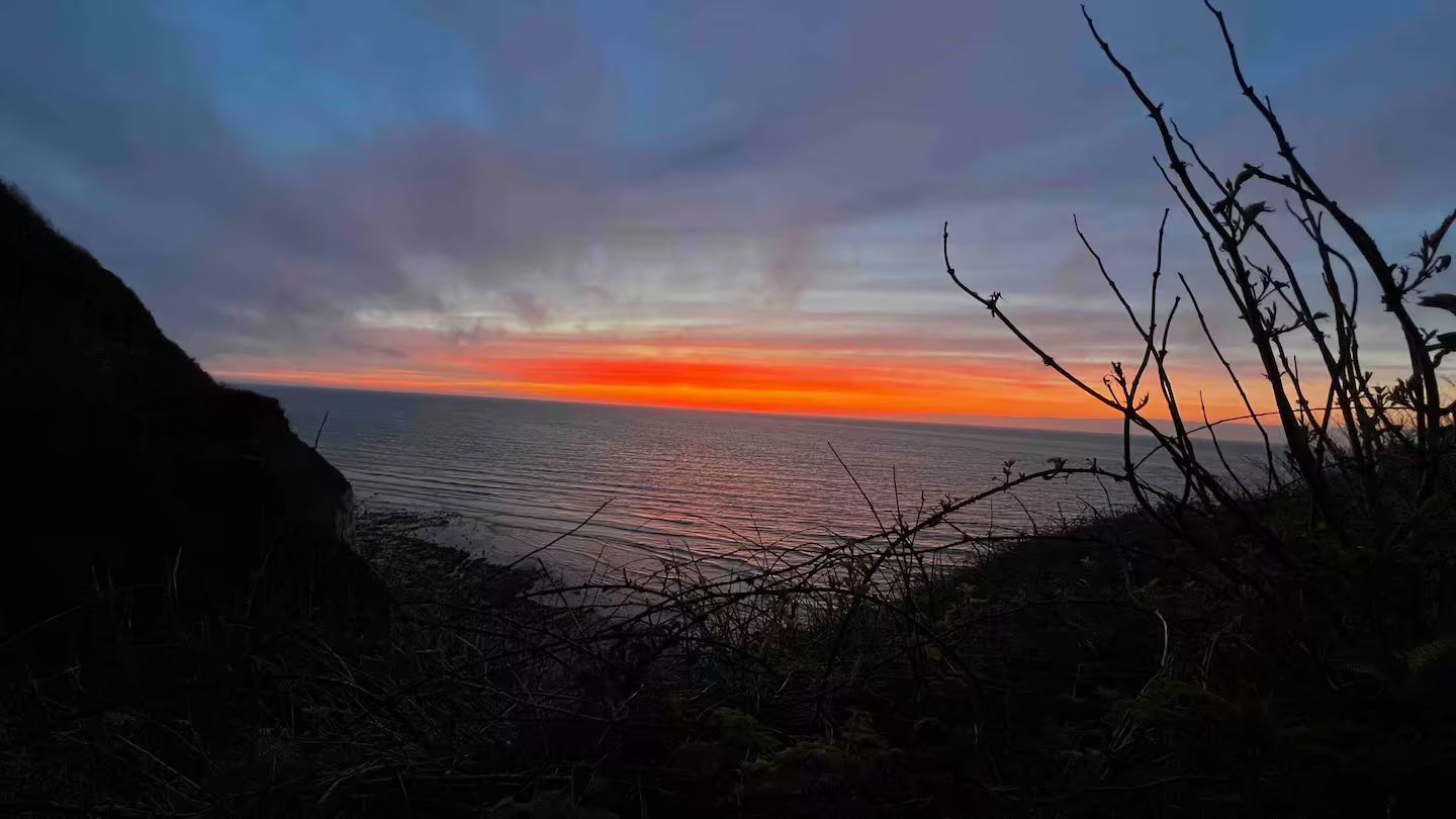 Un coucher de soleil sur l'océan avec une falaise au premier plan.