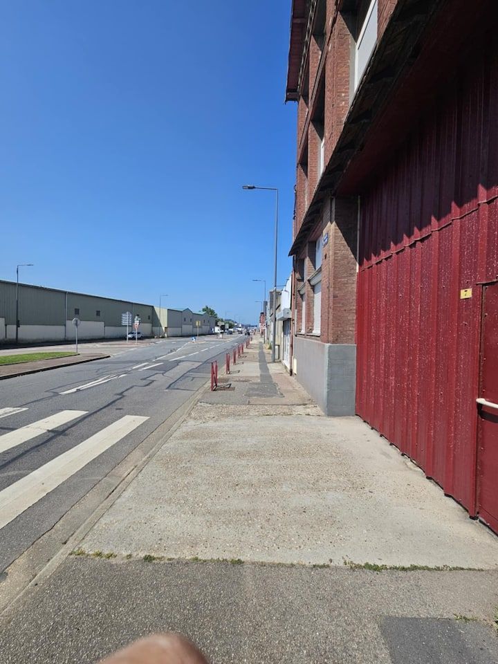 Trottoir désert à côté d'un bâtiment en briques rouges, dans une rue ensoleillée sous un ciel bleu.
